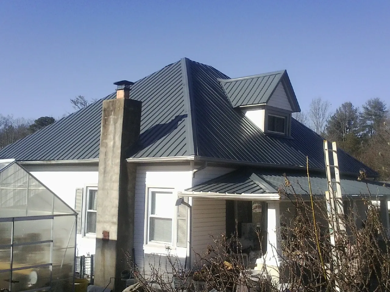 Dark blue standing seam metal roof on a white farmhouse with dormer — Slate & Tile Roof Repair by Roofing Brothers in Streamwood