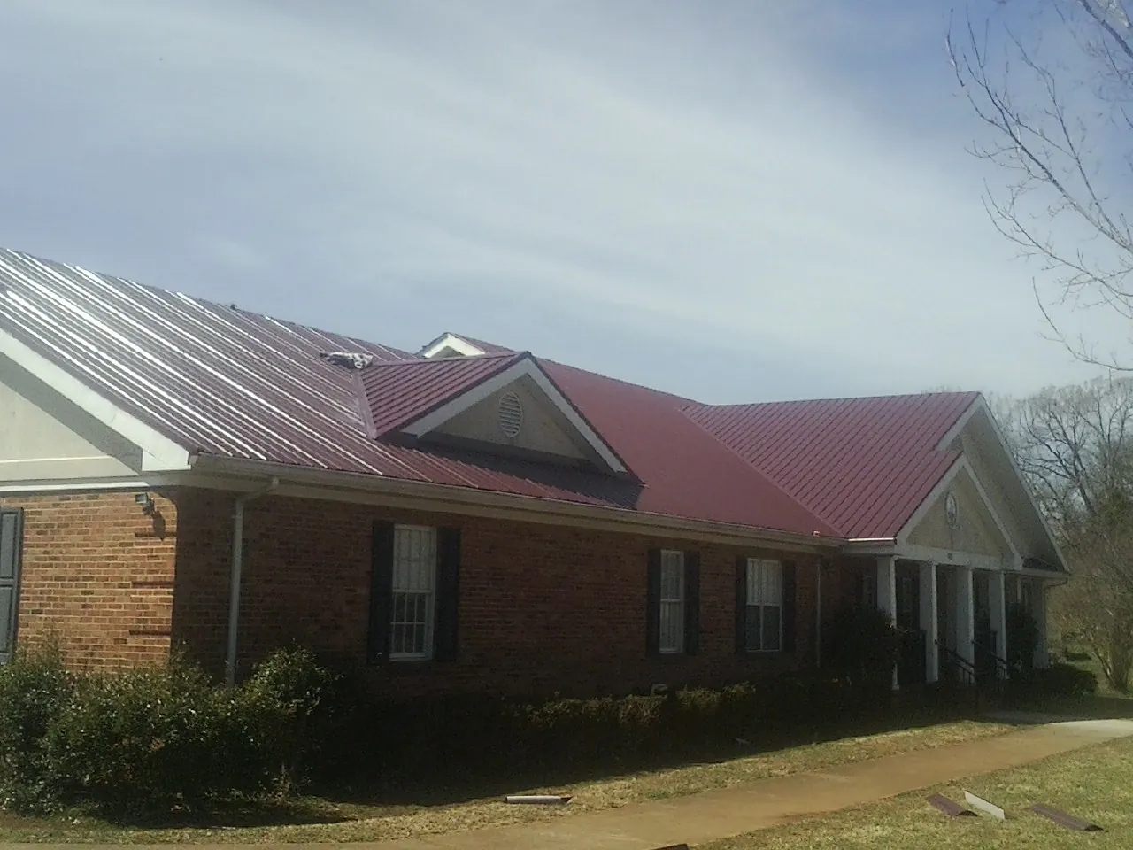 Red metal roof with gabled entries on a long brick building, from a Hail Damage Roof Repair job in Streamwood