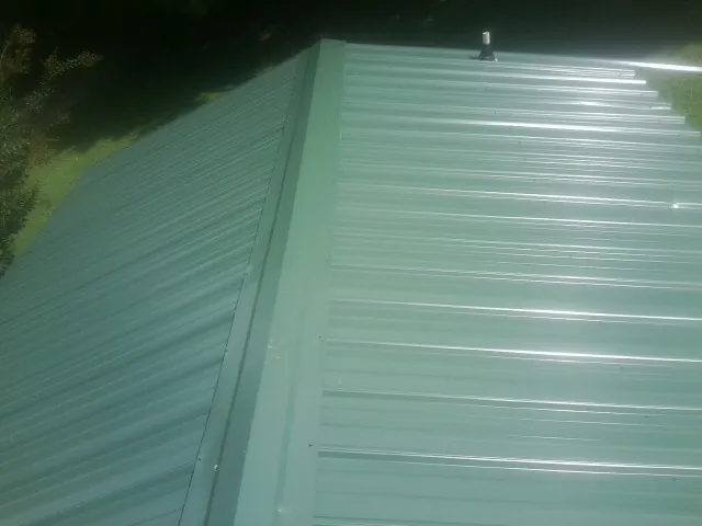 New green metal panels meeting at the ridge of a roof — Flat Roof Repair work by our crew in Streamwood