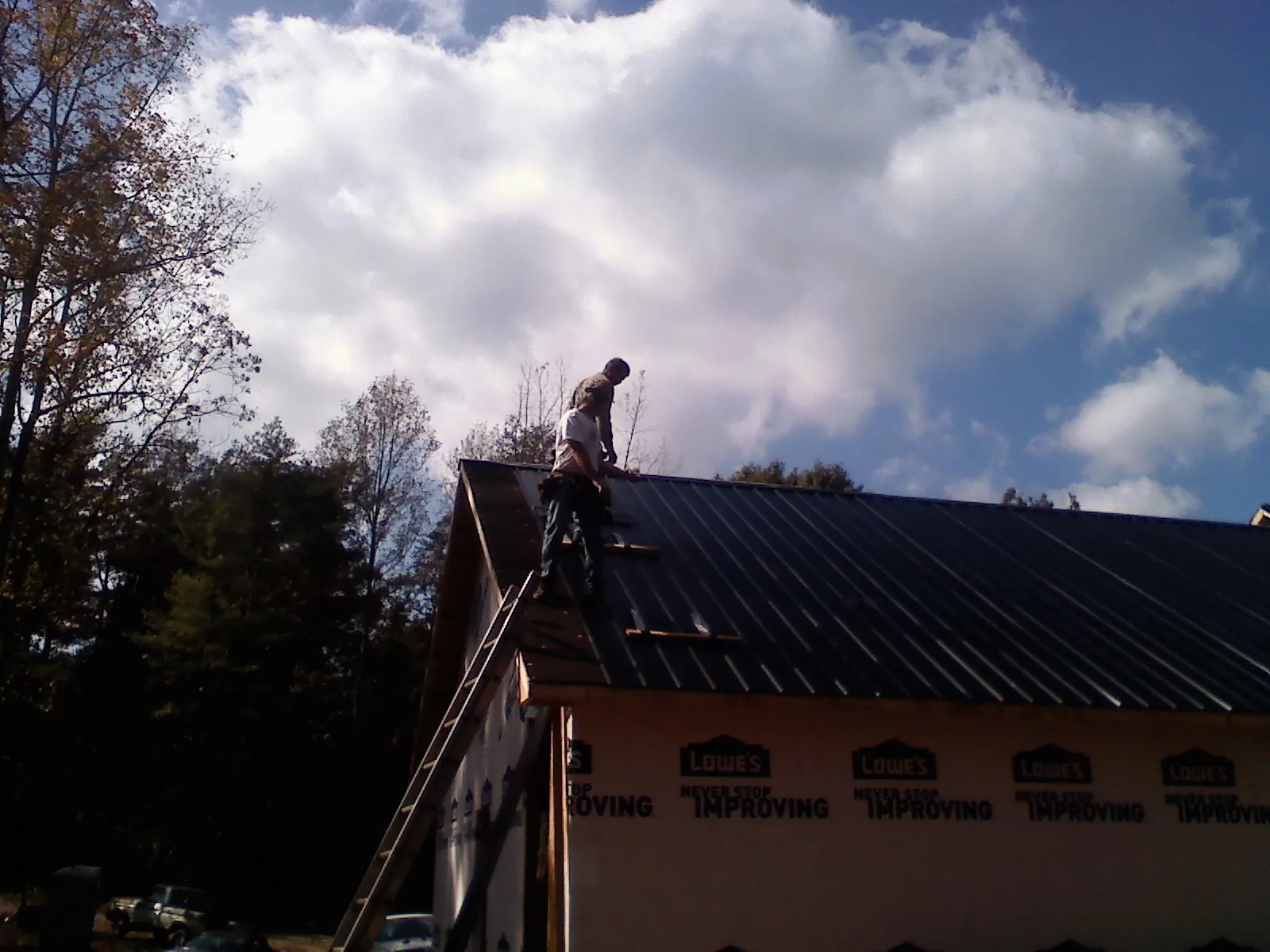 Roofer fastening dark metal panels high against a cloudy sky, from a Roof Inspection job in Streamwood