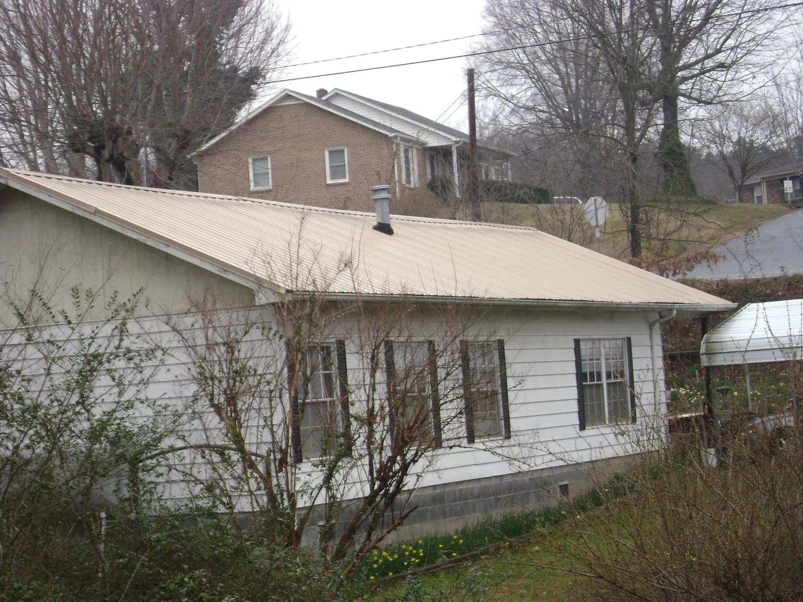 Tan metal roof on a white sided house set into a hillside — Commercial Roofing by Roofing Brothers in Streamwood